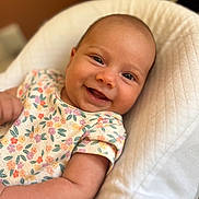 Lya a rejoint le concours — aidez-le/la à gagner de superbes lots ! baby, smile, face, infant, child, clothing, floral_pattern, skin, arm, cute, happy, person, portrait, seat, soft_texture, indoors, head, eyes, mouth, cheerful