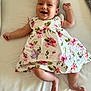 baby, infant, smiling, happy, floral_dress, white_background, lying_down, cute, child, skin, arm, leg, foot, head, face, playful, indoors, person, young_child, joyful