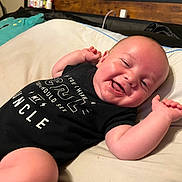 Osiris is registered to the contest to win money with this photo: baby, smiling, lying_down, black_clothing, bed, pillow, infant, happy, cute, child, skin, head, arm, hand, onesie, indoors, person, face, expression, resting