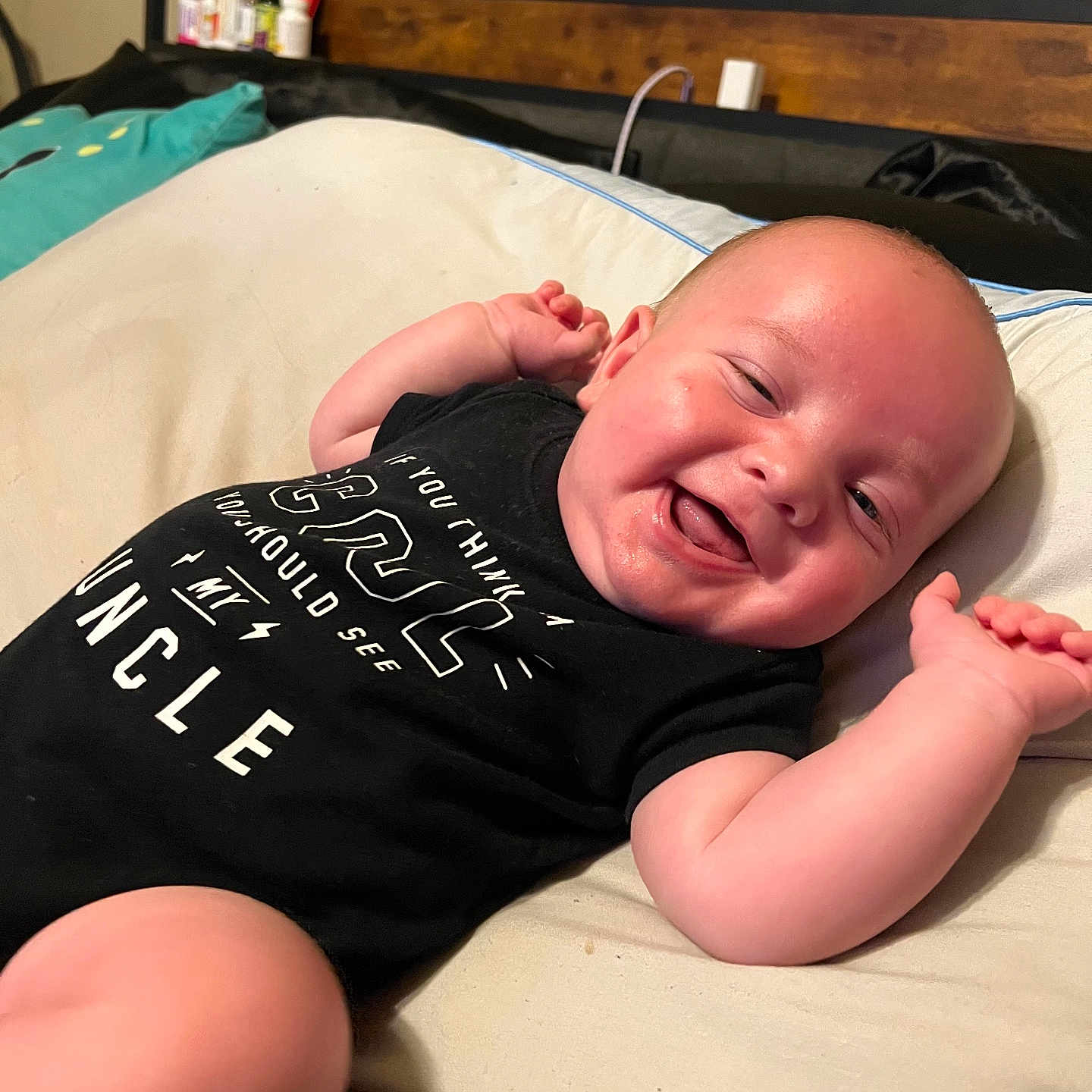 Osiris is registered to the contest to win money with this photo: arm, baby, bed, black_clothing, child, cute, expression, face, hand, happy, head, indoors, infant, lying_down, onesie, person, pillow, resting, skin, smiling