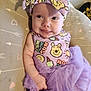 Josie is registered to the contest to win money with this photo: baby, child, purple, dress, headband, bow, smile, tongue, face, infant, patterned_clothing, cartoon_characters, cushion, heart_pattern, arrow_pattern, lying_down, cute, happy, indoors, tulle_skirt