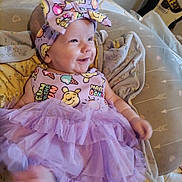 Josie joined the competition — help win amazing prizes! baby, smiling, headband, dress, purple, cartoon_print, cushion, blanket, indoor, infant, happy, person, foot, furniture, guitar, wooden_wall, patterned_clothing, tutu, cute, child