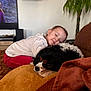 child, toddler, dog, pet, couch, blanket, sleeping, cozy, living_room, plant, television, pillow, fur, portrait, indoor, resting, home, snuggle, relaxed, family
