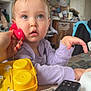 Iris participe au concours pour gagner de l'argent avec cette photo : child, toddler, toy_phone, remote_control, table, indoor, portrait, curiosity, big_eyes, purple_sweater, hand, face, eyes, wooden_cabinet, clutter, wall_photos, yellow_toy, playing, expression, household