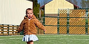 Iris participe au concours pour gagner de l'argent avec cette photo : child, toddler, walking, jacket, coat, dress, boots, astroturf, grass, playground, fence, building, sky, sunny, shadow, portrait, outdoor, daytime, person, play