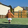 child, toddler, walking, jacket, coat, dress, boots, astroturf, grass, playground, fence, building, sky, sunny, shadow, portrait, outdoor, daytime, person, play