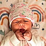 baby, newborn, infant, hat, clenched_fists, blanket, stars, rainbow, cute, sleepwear, face, portrait, child, soft_light, indoors, lying_down, patterned_clothing, peaceful, young, cozy