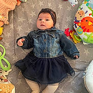 Mia participe au concours pour gagner de l'argent avec cette photo : baby, denim_jacket, skirt, headband, toys, playmat, star_pattern, infant, cute, lying_down, colorful, soft_toys, child, indoors, legs, face, clothing, happy, toddler, portrait