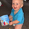 toddler, child, blue_shirt, kneeling, carpet, snack, cheez_it, can, crumbs, happy, indoor, smile, face, food, playful, person, floor, casual, cute, messy