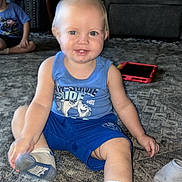 Carter joined the competition — help win amazing prizes! adult, blue_shirt, carpet, casual, child, floor, furniture, happy, home, indoor, living_room, person, playtime, seated, shorts, smiling, socks, tablet, toddler, toy_dinosaur
