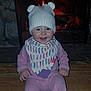 baby, child, smiling, hat, knit_hat, bear_ears, pajamas, pink_clothing, bib, floor, wood_floor, fireplace, fire, warmth, indoors, cute, infant, sitting, face, cozy