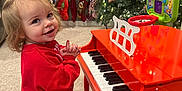 Summer is registered to the contest to win money with this photo: barefoot, carpet, child, christmas_tree, cute, festive, furniture, happy, holiday_decor, home, indoor, playing, red_piano, red_sweater, smiling, stockings, stool, toddler, toy_piano, young_child