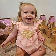 Summer is registered to the contest to win money with this photo: baby, carpet, child, cute, eleven_months, hair_ponytail, happy, heart_sign, indoor, infant, person, pink_clothing, playtime, portrait, room, sitting, smiling, toddler, toy, wooden_dollhouse