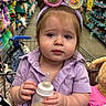 toddler, child, shopping_cart, bottle, milk, bunny_ears, headband, purple_clothing, stuffed_animals, toys, store_aisle, aisle_shelves, shopping, baby, indoor, cute, holding, person, face, expression