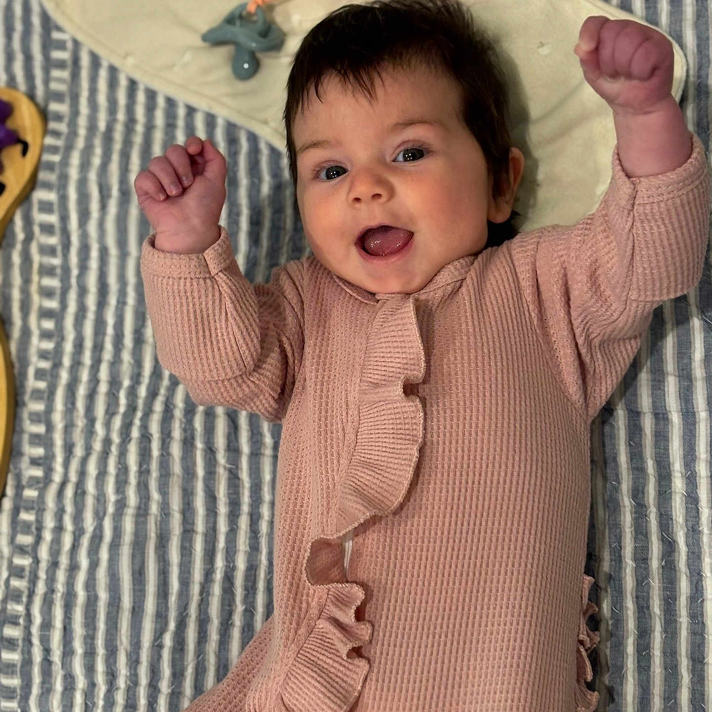 Sam Marie joined the competition — help win amazing prizes! baby, baby_accessory, child, closeup, clothing, cute, face, happy, indoors, infant, lying_down, pacifier, person, pink_onesie, portrait, raised_fists, ruffles, smiling, soft_texture, striped_blanket