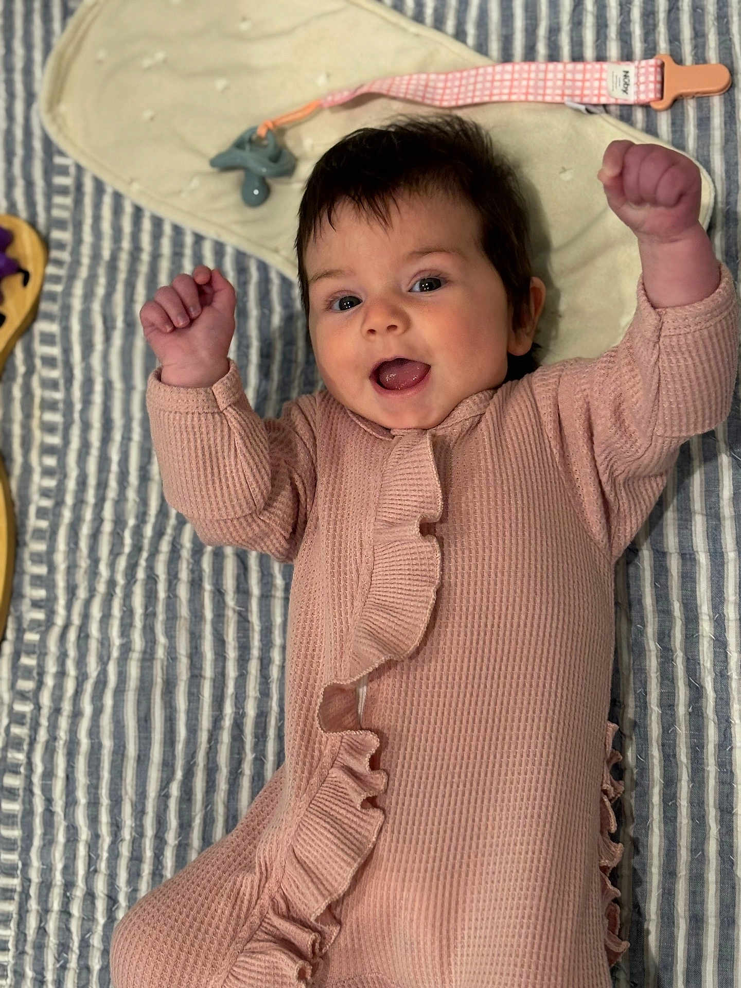 Sam Marie joined the competition — help win amazing prizes! baby, infant, pink_onesie, ruffles, smiling, happy, raised_fists, lying_down, striped_blanket, pacifier, clothing, face, person, cute, child, indoors, soft_texture, baby_accessory, closeup, portrait