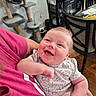 arm, baby, cabinet, cat_tree, child, clothing, cute, dining_chair, face, happy, holding, home, indoor, infant, person, pink_shirt, portrait, smiling, table, wooden_floor