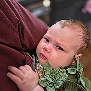 Anne joined the competition — help win amazing prizes! baby, child, closeup, clothing, cute, expression, eyes, face, green_flower, hand, head, holding, indoor, infant, maroon, person, portrait, skin, sleeve, young