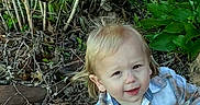 Joshua is registered to the contest to win money with this photo: toddler, child, plaid_shirt, shorts, sitting, sidewalk, plants, greenery, twigs, outdoor, curious, playful, blond_hair, casual_clothing, nature, daylight, young_child, person, smiling, shoes