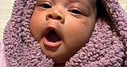 Jada joined the competition — help win amazing prizes! baby, child, face, blanket, purple, wrapped, cozy, expression, mouth_open, hand, ring, skin, eyelashes, indoor, closeup, soft_texture, warm, portrait, infant, curious