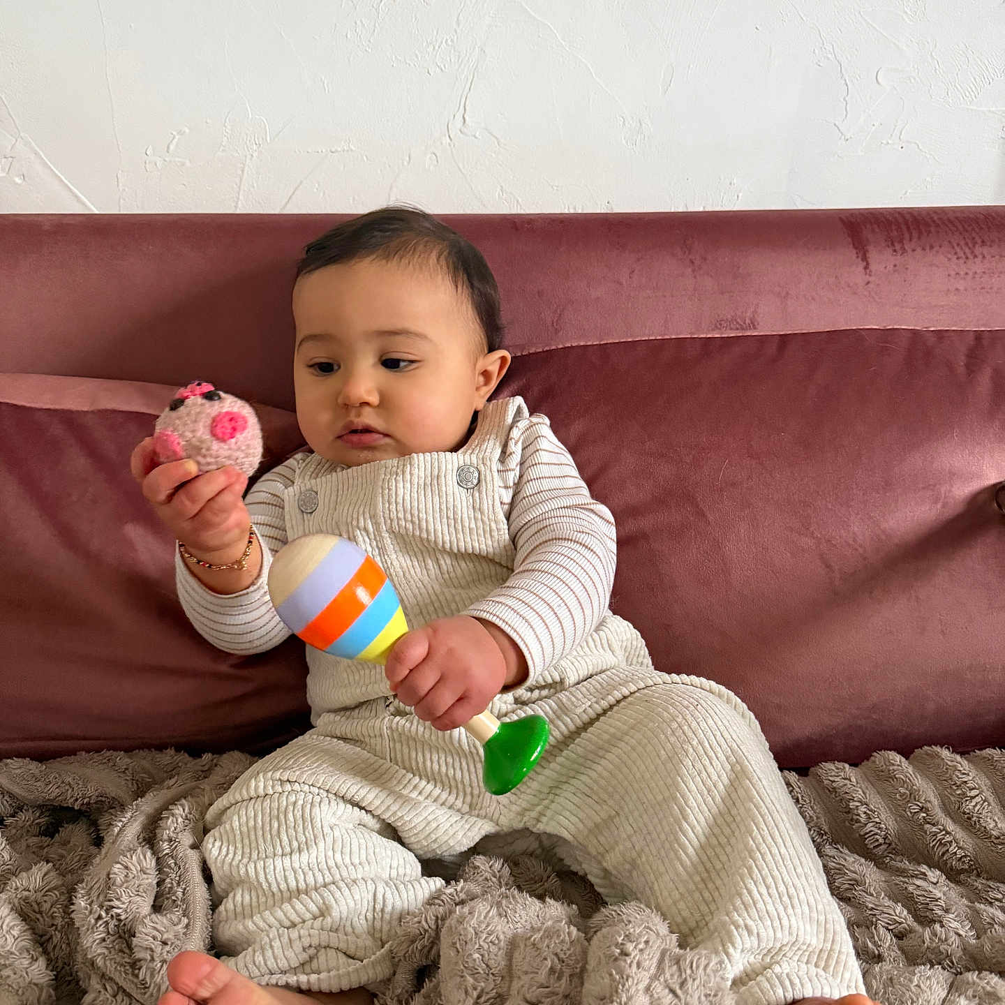 Kai participe au concours pour gagner de l'argent avec cette photo : baby, barefoot, blanket, bracelet, child, couch, cozy, curiosity, fabric_texture, face, head, indoor, infant, maraca, plush_toy, portrait, romper, sitting, striped_sleeves, toy_ball
