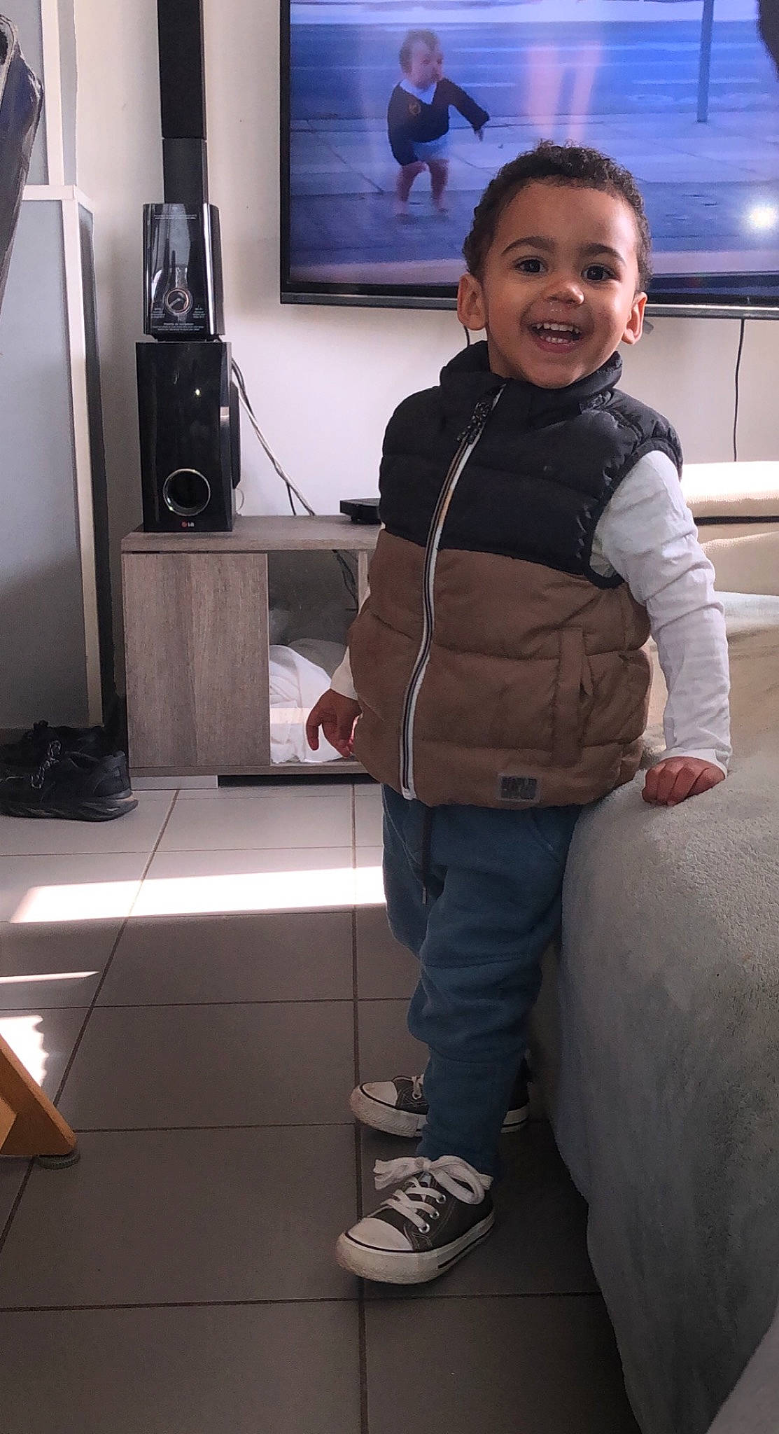 Junior participe au concours pour gagner de l'argent avec cette photo : audio_equipment, baby_toddler_clothing, comfort, electronic_device, floor, flooring, gadget, home_appliance, joint, joy, output_device, person, shoe, shoulder, smile, sneakers, standing, technology, television, television_set