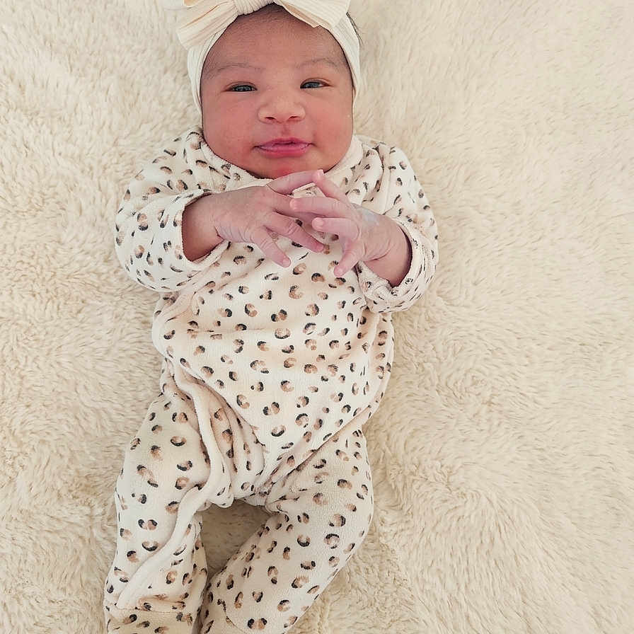Aïvy a rejoint le concours — aidez-le/la à gagner de superbes lots ! baby, infant, bow, headband, leopard_print, onesie, clothing, blanket, soft_texture, cute, child, portrait, smiling, hands, footed_pajamas, lying_down, indoor, newborn, skin, face