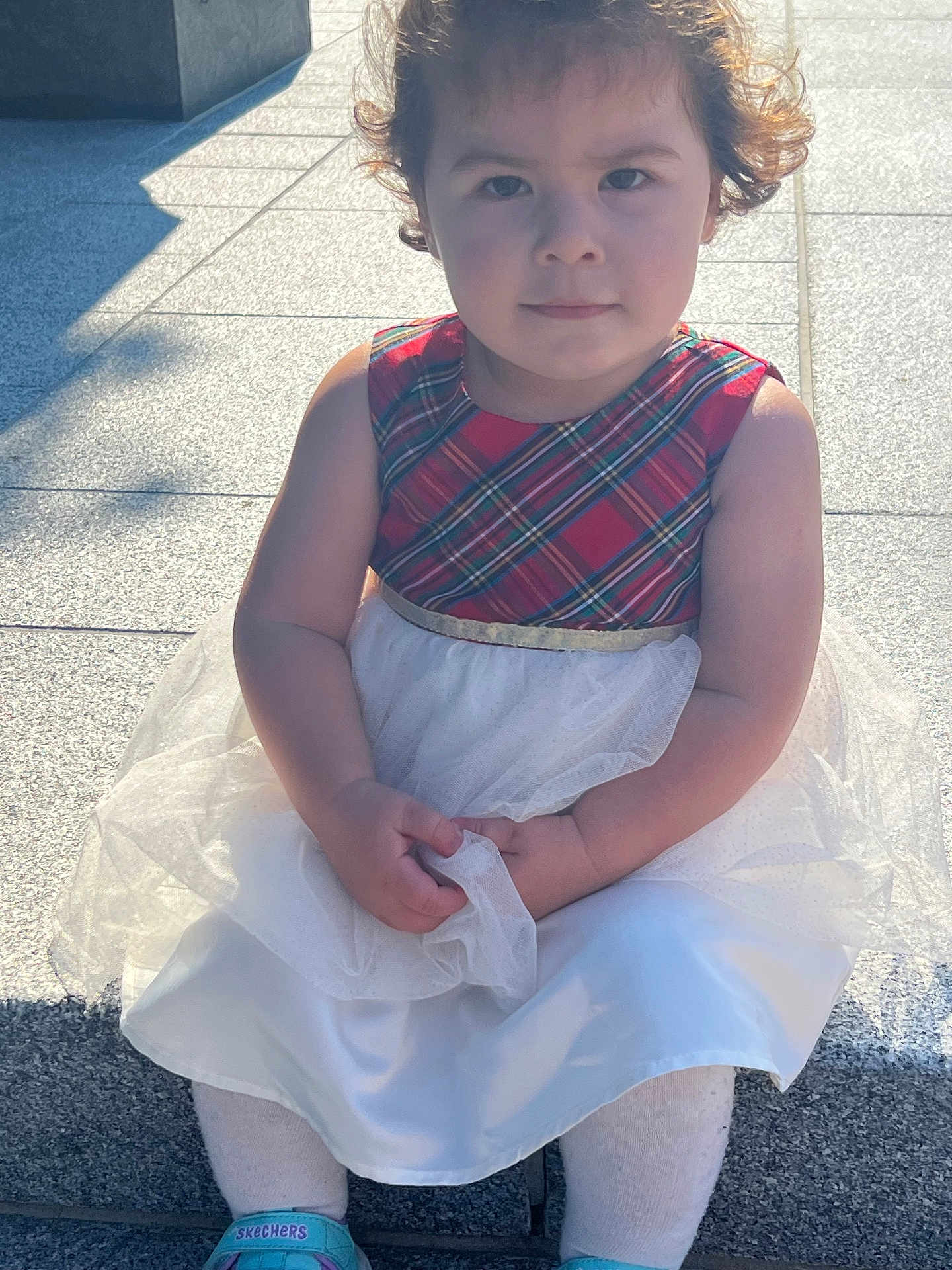 Angela Ademi joined the competition — help win amazing prizes! toddler, child, dress, plaid, white_tulle, curly_hair, sitting, outdoor, stone_steps, sunlight, shadow, serious_face, shoes, socks, person, portrait, daylight, young_child, casual, fashion