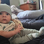 Dominick joined the competition — help win amazing prizes! baby, child, beanie, toy, hand, sitting, pillow, bed, clothing, socks, indoor, person, face, cute, infant, soft_toy, casual, relaxed, young, portrait