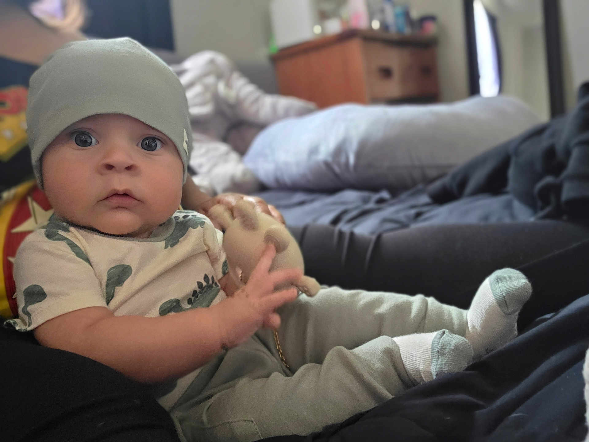 Dominick joined the competition — help win amazing prizes! baby, child, beanie, toy, hand, sitting, pillow, bed, clothing, socks, indoor, person, face, cute, infant, soft_toy, casual, relaxed, young, portrait