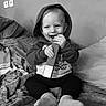 bed, black_and_white, blanket, child, clothing, cozy, cute, face, happy, hoodie, indoor, monochrome, person, playful, portrait, sitting, smile, socks, toddler, young_child