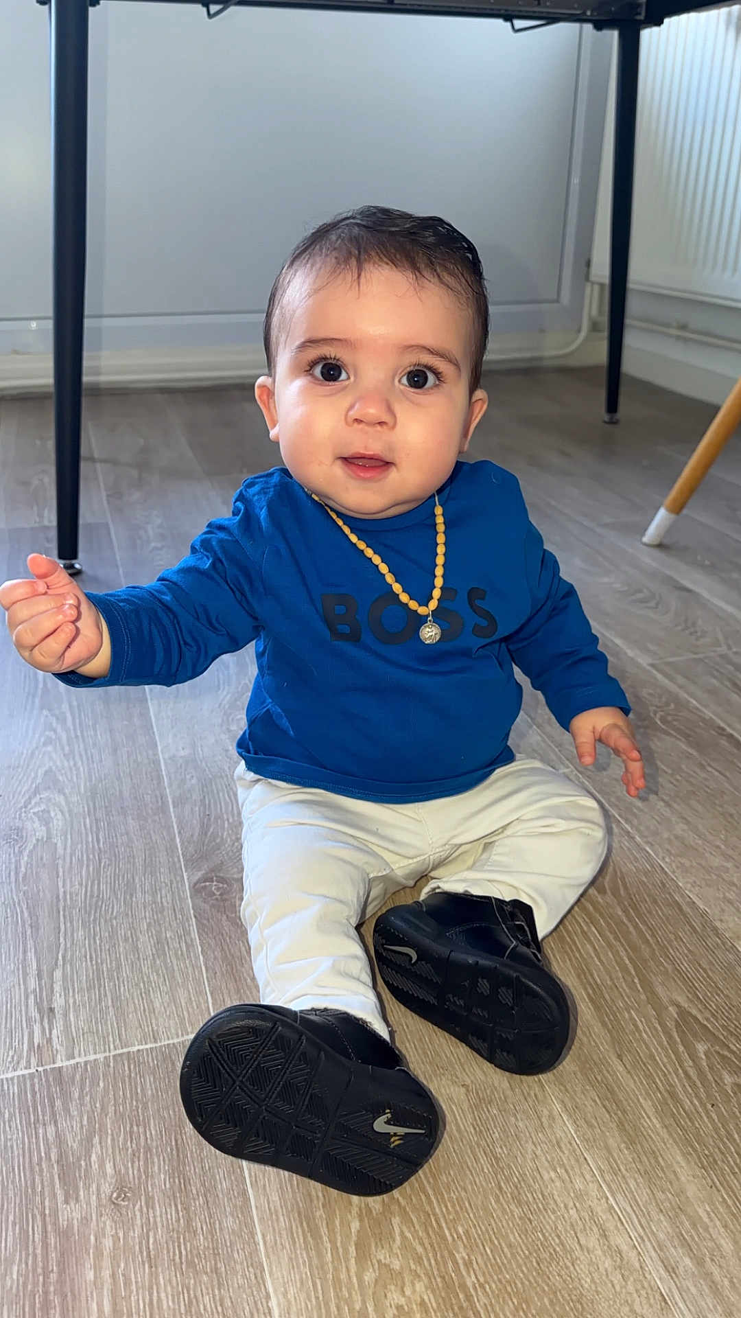 Dgezym a rejoint le concours — aidez-le/la à gagner de superbes lots ! baby, child, floor, blue_shirt, white_pants, black_shoes, necklace, indoor, wooden_floor, cute, sitting, person, young_child, expression, looking, footwear, flooring, home, furniture, legs