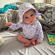 Alessia joined the competition — help win amazing prizes! baby, infant, child, bed, blanket, hat, floral_print, onesie, barefoot, feet, sitting, portrait, big_eyes, blue_eyes, toy_book, bedroom, cozy, cute, curious_gaze, soft_light