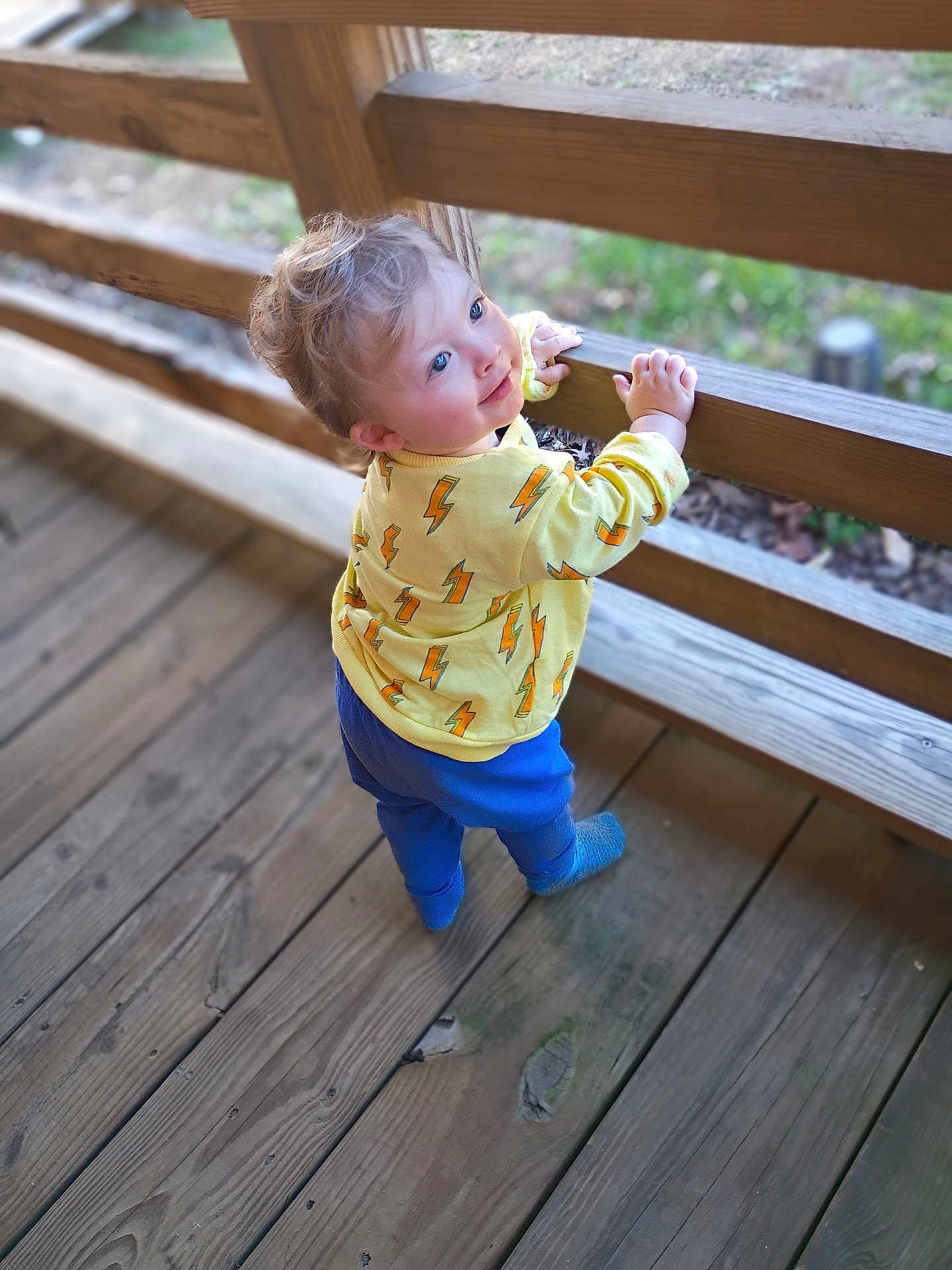 Asher joined the competition — help win amazing prizes! toddler, child, yellow_sweater, lightning_bolt_pattern, blue_pants, blue_eyes, blonde_hair, wooden_deck, wooden_railing, outdoor, standing, smiling, curious, daylight, casual_clothing, portrait, baby, person, happy, playful