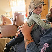 Asher joined the competition — help win amazing prizes! baby, child, man, beard, tattoo, cap, backwards_cap, indoor, furniture, chair, window, sunlight, shirtless, person, holding, casual_clothing, curious, smile, home, relaxed