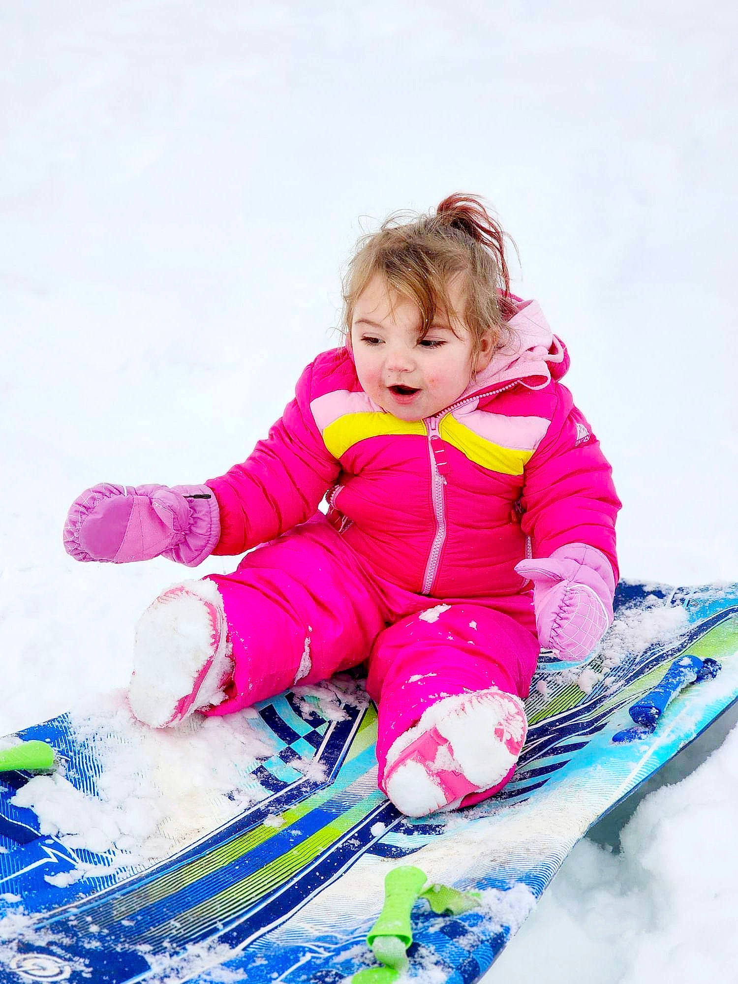 Gunner is registered to the contest to win money with this photo: baby_toddler_clothing, face, fun, glove, happy, ice_cap, jacket, leisure, magenta, person, personal_protective_equipment, recreation, sled, sledding, sleeve, slope, snow, toddler, vehicle, winter