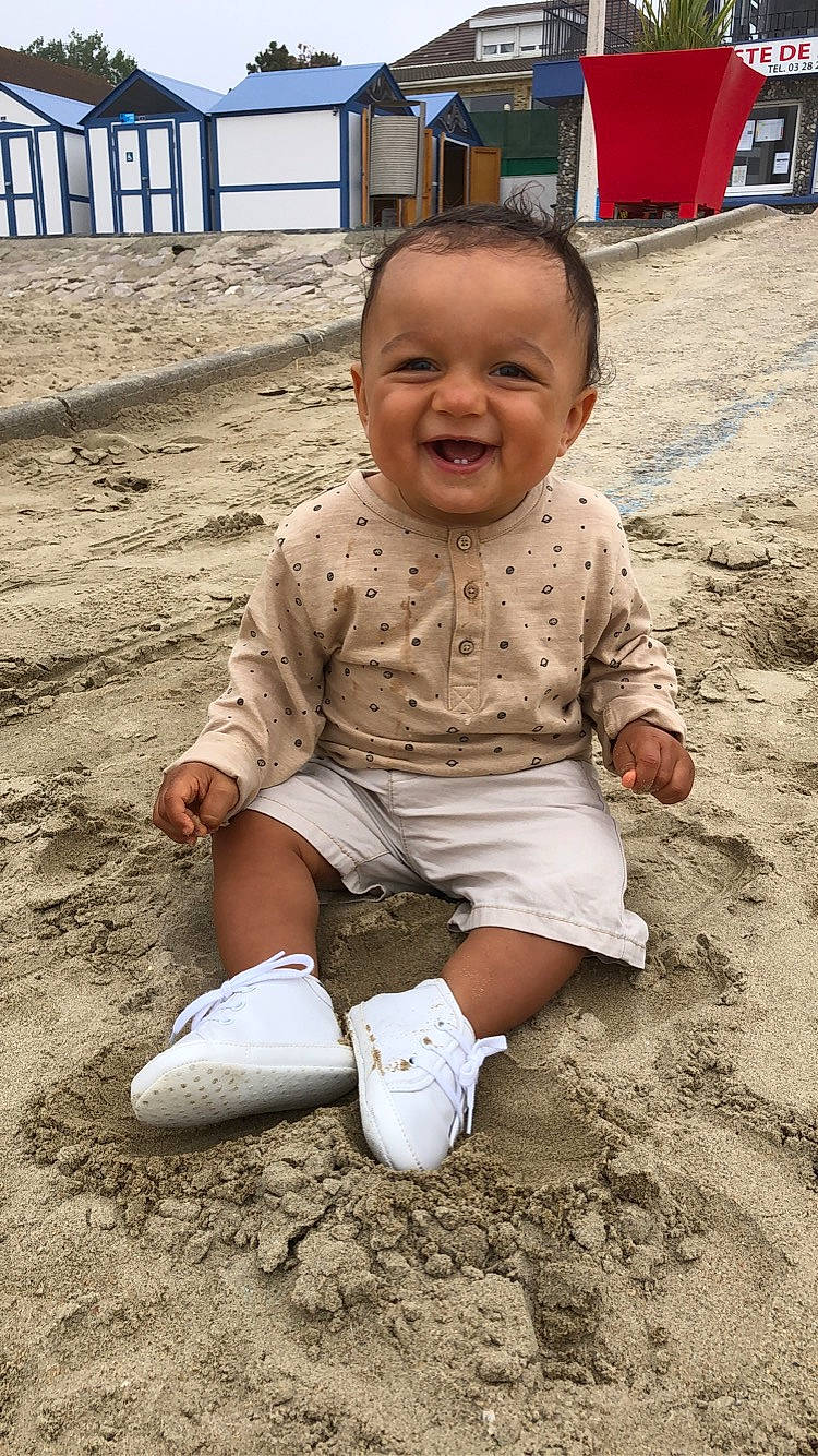 Marwan a rejoint le concours — aidez-le/la à gagner de superbes lots ! baby, baby_laughing, baby_toddler_clothing, cheek, child, eye, face, joy, laugh, mouth, nose, person, sand, sleeve, sock, toddler, tongue, walking_shoe
