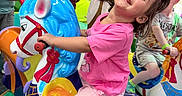 Nadiyah Claire is registered to the contest to win money with this photo: child, toddler, carousel, indoor_play_area, colorful, horse, smiling, joyful, pink_shirt, playground, fun, riding, toy, amusement, happy, person, play, background, socks, hair_bow
