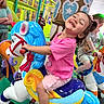 amusement, background, carousel, child, colorful, fun, hair_bow, happy, horse, indoor_play_area, joyful, person, pink_shirt, play, playground, riding, smiling, socks, toddler, toy