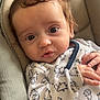 baby, child, close_up, clothing, comfort, curly_hair, cushion, cute, dinosaur_print, hand, indoors, infant, pajamas, portrait, resting, seat, skin, soft_lighting, wide_eyes, young