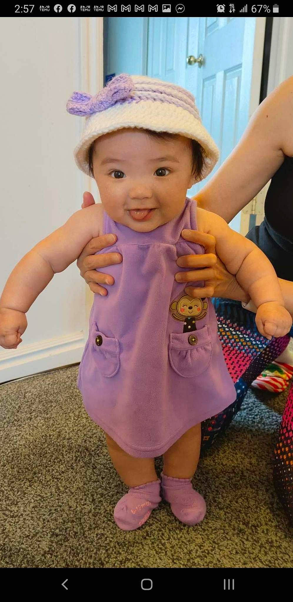 Marlee is registered to the contest to win money with this photo: baby, baby_toddler_clothing, cap, child, dress, finger, fun, gesture, hand, happy, hat, headwear, magenta, nail, person, pink, purple, skin, sleeve, smile