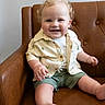 toddler, child, smiling, blonde_hair, curly_hair, shirt, shorts, sitting, leather_chair, indoor, happy, cute, portrait, baby, furniture, casual_clothing, skin, face, person, young_child