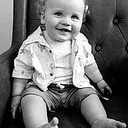 Jackson joined the competition — help win amazing prizes! toddler, child, smile, happy, curly_hair, shirt, shorts, barefoot, chair, leather, tufted, black_and_white, portrait, seated, indoor, cute, baby, person, candid, expression