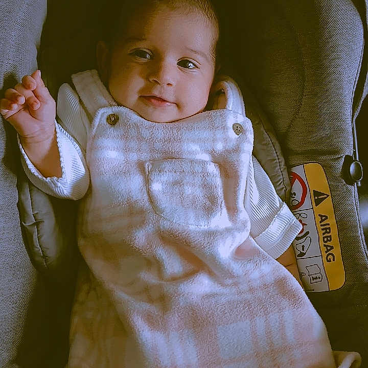 Yashnoor is registered to the contest to win money with this photo: baby, car_seat, child, clothing, comfort, cushion, cute, dress, eyes, face, happy, indoors, infant, pink, portrait, small_hand, smile, soft_lighting, white, young