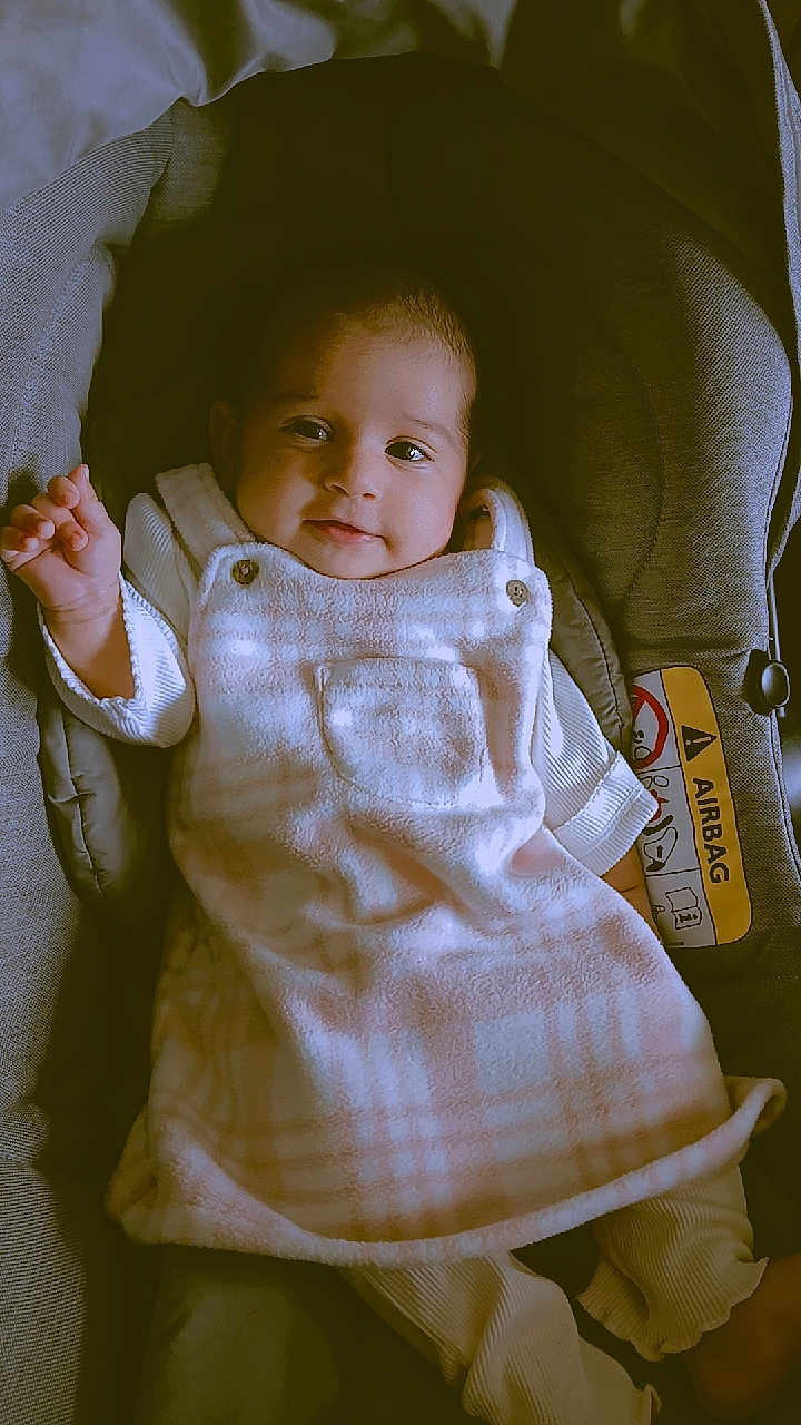 Yashnoor is registered to the contest to win money with this photo: baby, car_seat, child, clothing, comfort, cushion, cute, dress, eyes, face, happy, indoors, infant, pink, portrait, small_hand, smile, soft_lighting, white, young