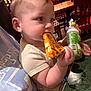 Bentley is registered to the contest to win money with this photo: baby, child, pizza, food, drink, sippy_cup, restaurant, table, chair, person, indoor, eating, cute, blond_hair, blue_eyes, casual_clothing, hand, face, seat, dining