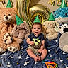 baby, balloons, birthday, blanket, bunny, cat_plush, celebration, child, cow_plush, indoors, infant, panda, party_hat, portrait, rattle, sitting, smiling, stuffed_animals, teddy_bear, toy