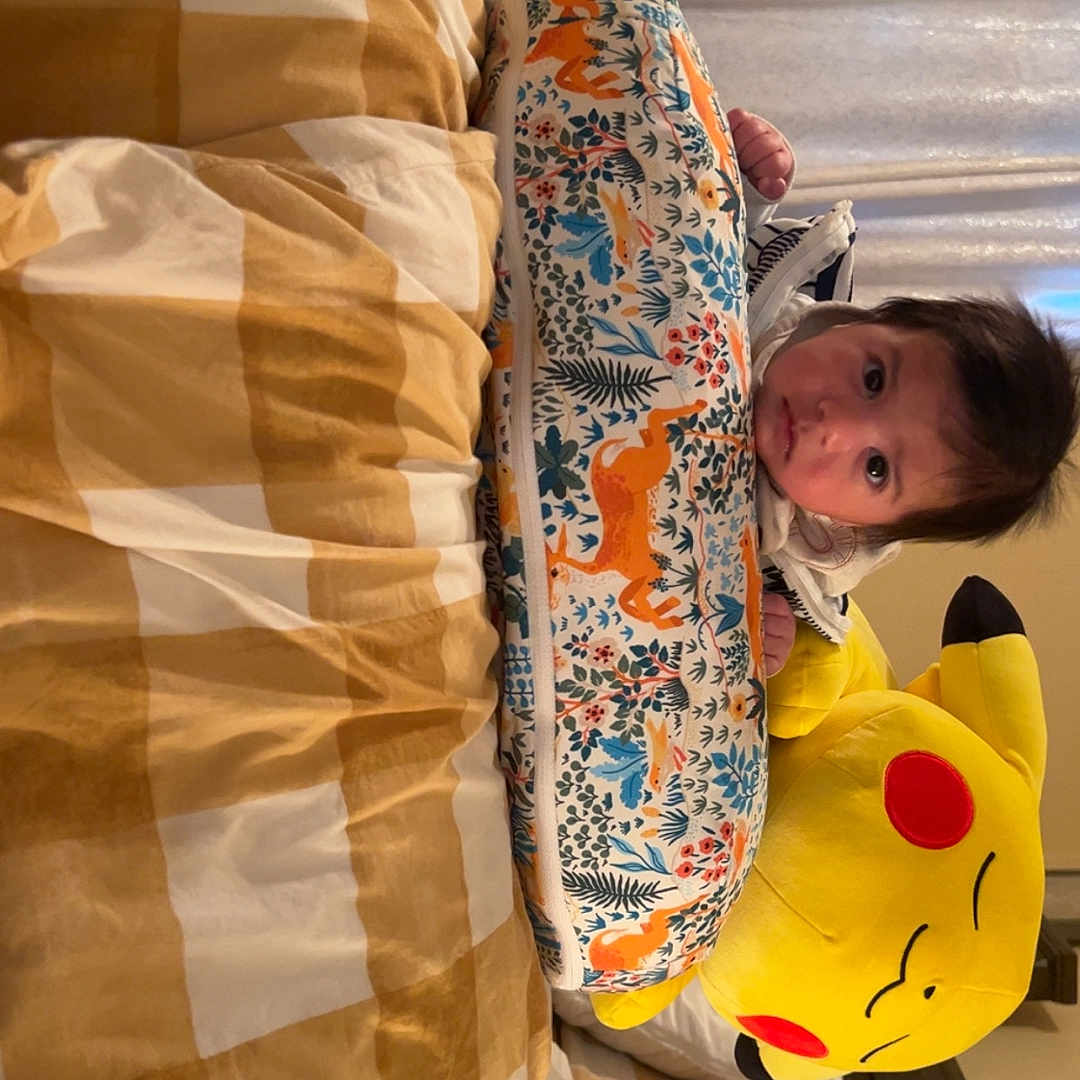 Oliver is registered to the contest to win money with this photo: animal_print, baby, bed, blanket, child, colorful, cozy, curtains, cushion, expression, face, furniture, head, indoor, infant, person, pikachu, plush_toy, soft, stuffed_animal