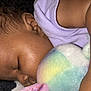 baby, sleeping, plush_toy, close_up, curly_hair, purple_clothing, blanket, infant, peaceful, toddler, face, arm, soft_texture, cute, resting, child, indoors, napping, skin, cozy