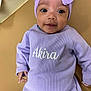 baby, infant, child, lavender, headwrap, clothing, smile, face, portrait, cute, laying_down, soft_surface, earrings, long_sleeve, small_hands, young_child, indoors, person, apparel, baby_girl